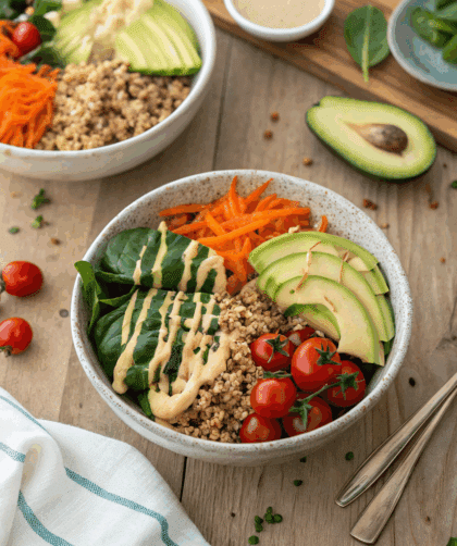 spelt and quinoa grain bowls topped with sliced avocado, cherry tomatoes, baby spinach, grated carrot, and tahini drizzle.