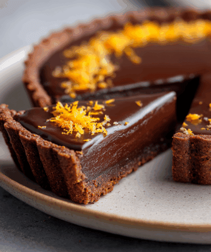 Side-angle close-up of a sliced Spelt Orange and Dark Chocolate Tart, showing the crisp spelt crust and smooth dark chocolate interior. Slice pulled slightly forward.