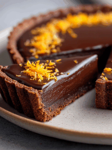 Side-angle close-up of a sliced Spelt Orange and Dark Chocolate Tart, showing the crisp spelt crust and smooth dark chocolate interior. Slice pulled slightly forward.