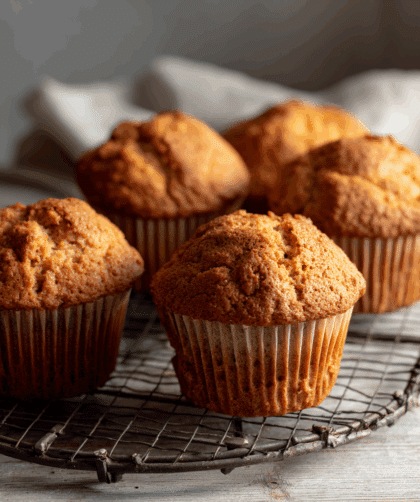Freshly baked spelt breakfast muffins, batch of six, golden tops, soft crumb texture, placed on a wire cooling rack on a light wooden table.