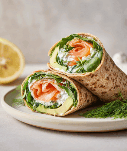 A neatly sliced spelt wrap filled with smoked salmon, avocado slices, spinach, Greek yogurt, dill, and lemon.