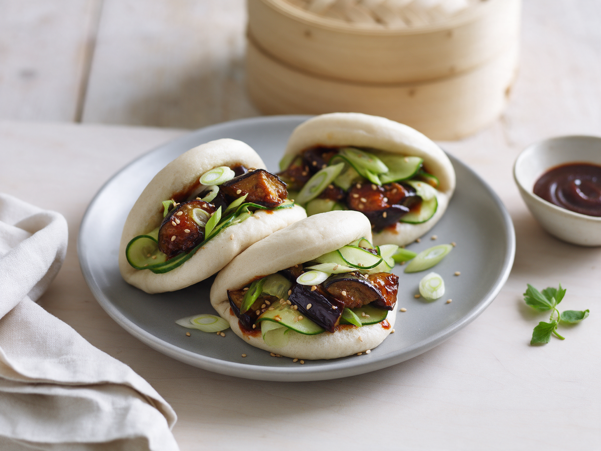 Open spelt steamed buns filled with glossy hoisin aubergine and cucumber on a grey ceramic plate