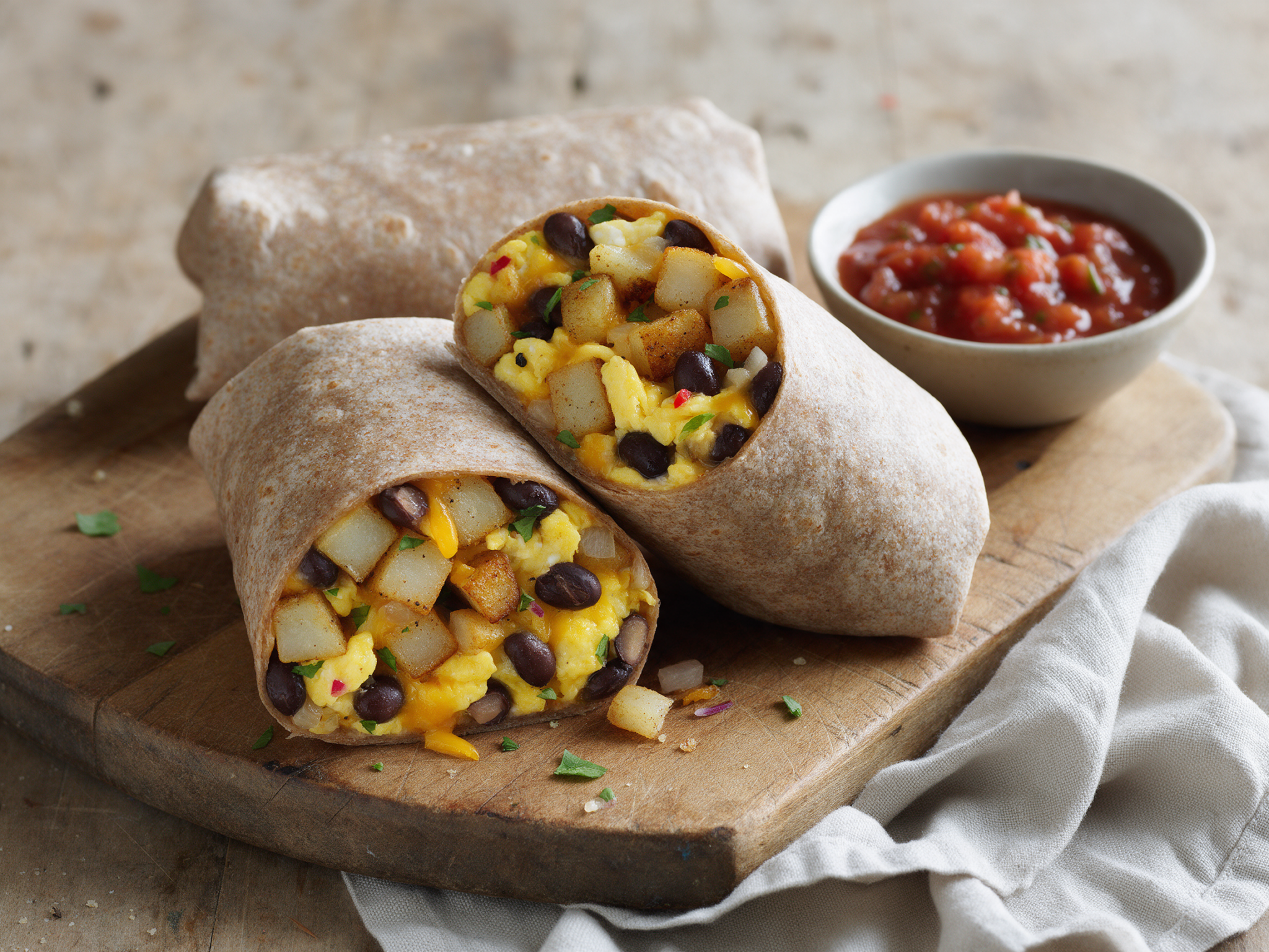 Halved spelt breakfast burrito showing eggs, black beans, and crispy potato cubes on a wooden board